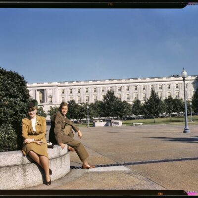 1943. On maneuvers in wartime Washington. "A soldier and a woman in a park, with the Old [Russell] Senate Office Building behind them." 4x5 Kodachrome transparency, photographer unknown. Office of War Information.