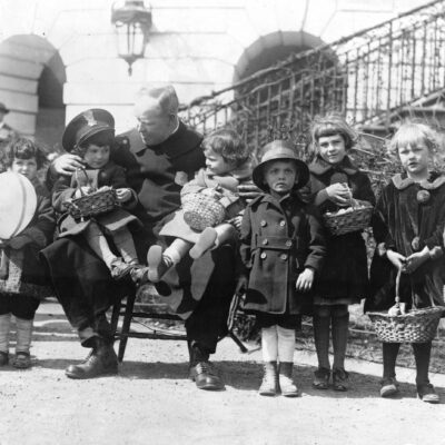 Officer Edgar E. Porter, full-length portrait, seated on a chair, holding two children on his lap and with several children standing to his right and left during the annual White House Easter egg roll.