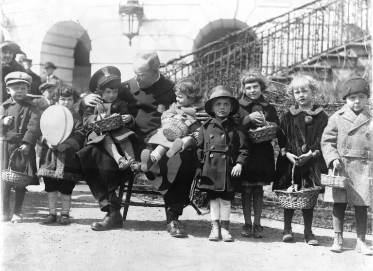 Officer Edgar E. Porter, full-length portrait, seated on a chair, holding two children on his lap and with several children standing to his right and left during the annual White House Easter egg roll.