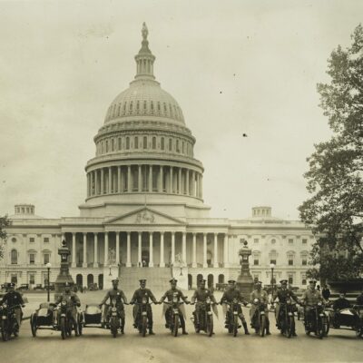 Photograph shows a group of motorcycle policemen, from left to right: "Sergt. J.E. Boyle, L.F. Reilly, W.D. Vaughn, F.S. Tyser, L.D. Redman, D.E. Gailmore, G.P. Waite, R.H. Mansfield, G.M. Little, A. Shockey, W.C. Lewis, [and] Capt. J.A. Abbott" with view of the U.S. Capitol in the background.