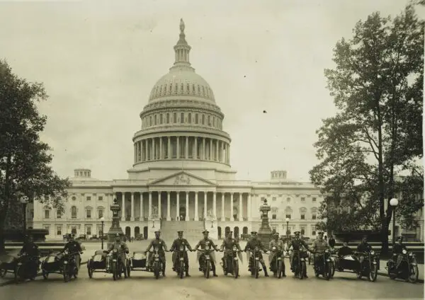 Photograph shows a group of motorcycle policemen, from left to right: "Sergt. J.E. Boyle, L.F. Reilly, W.D. Vaughn, F.S. Tyser, L.D. Redman, D.E. Gailmore, G.P. Waite, R.H. Mansfield, G.M. Little, A. Shockey, W.C. Lewis, [and] Capt. J.A. Abbott" with view of the U.S. Capitol in the background.
