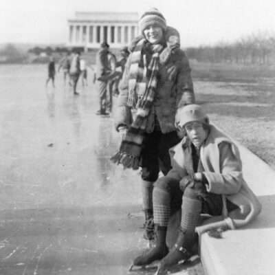 Abbey Jackson, seated, and Celene DuPuy ice skating on reflecting pool, with Lincoln Memorial in background