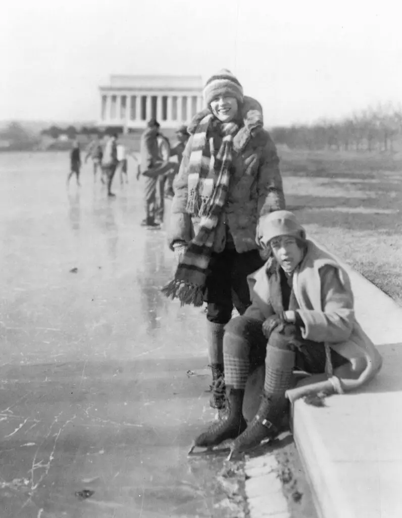 Abbey Jackson, seated, and Celene DuPuy ice skating on reflecting pool, with Lincoln Memorial in background