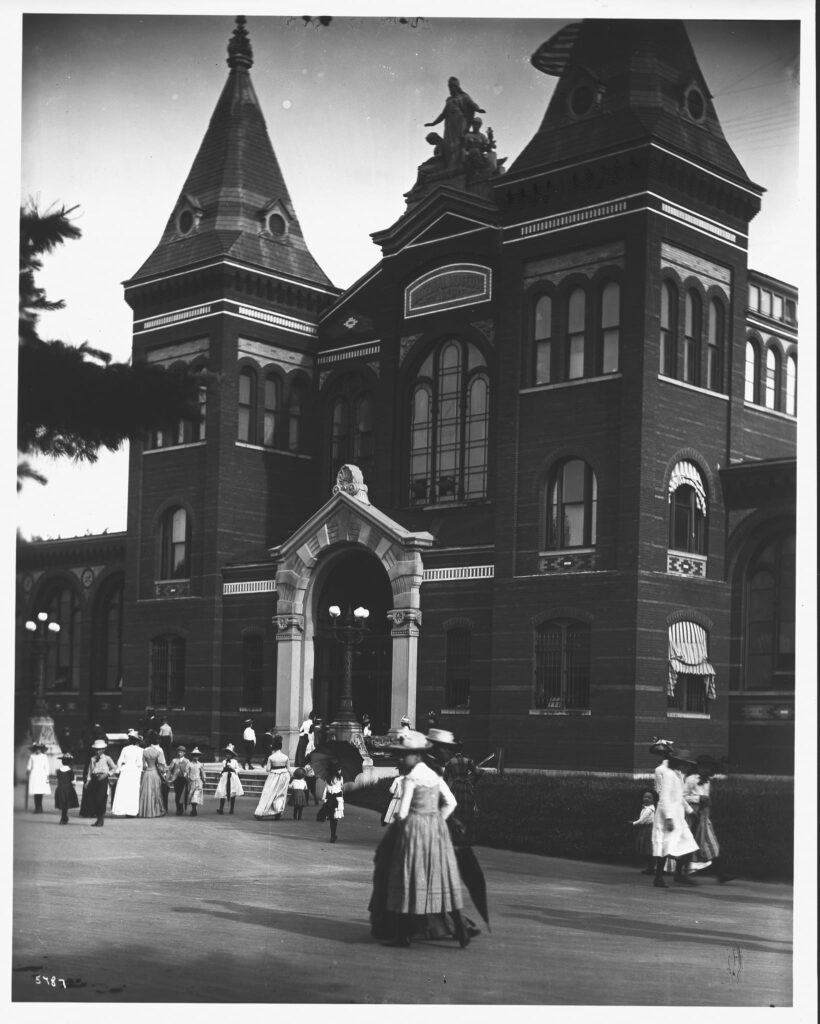 At the turn of the century, visitors are entering and leaving the United States National Museum Building, now Arts and Industries Building, via the North Entrance. The entrance has glass doors, which dates it to before the Hornblower and Marshall designed doors installed between 1902-1907