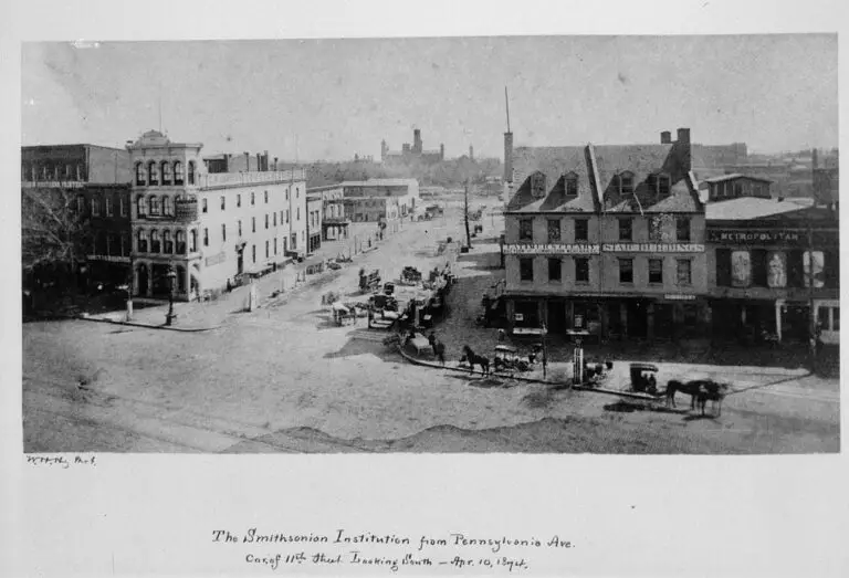 Looking south from the corner of Pennsylvania Avenue and 11th Street, the silhouette of the Smithsonian Institution Building is seen in the distance. The photograph, taken by William Henry Holmes and signed "W.H.H. Phot.," shows horse-drawn carriages along the avenue of storefronts. Above the first building to the right of 11th Street, the sign reads "Latimer & Cleary Auction and Commission Merchants", the next building has a sign "Star Buildings," and the third building "Metropolitan."