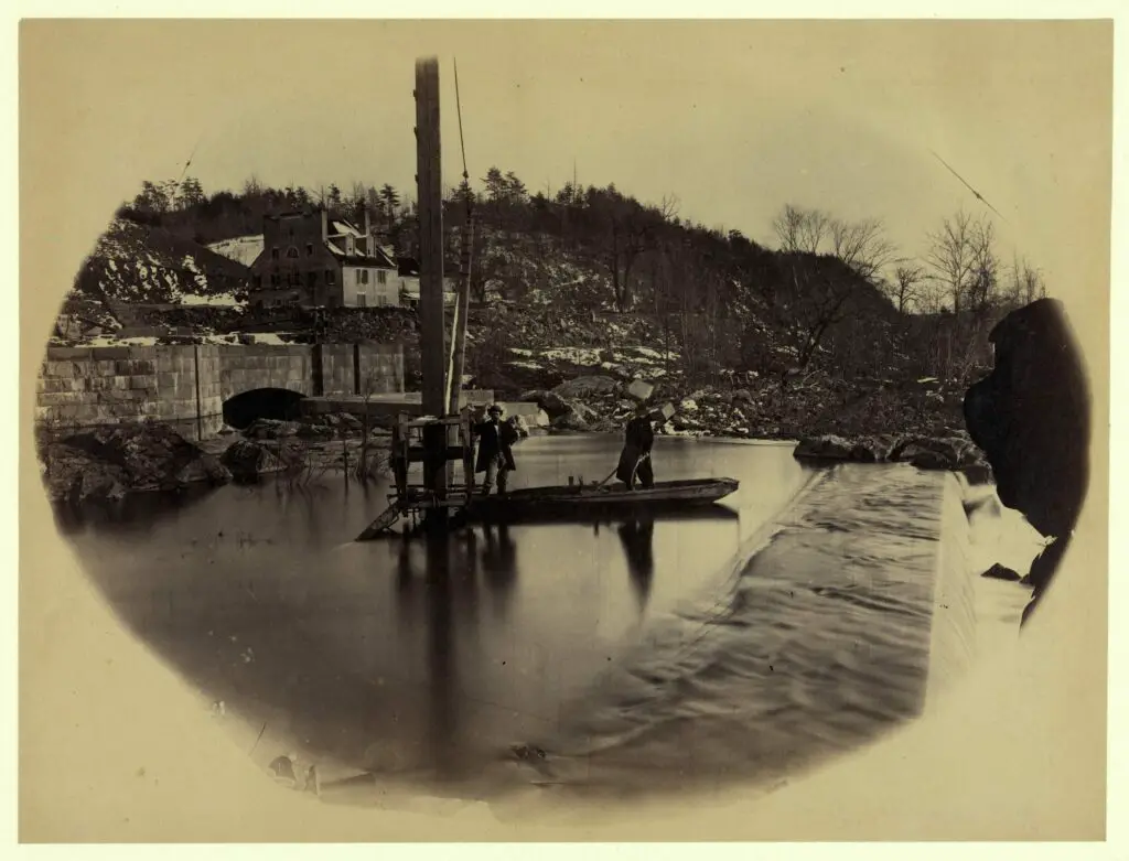 Entrance to Washington Water Works, Great Falls, Potomac River - Photograph shows two men standing in a small flat boat near the spillway.