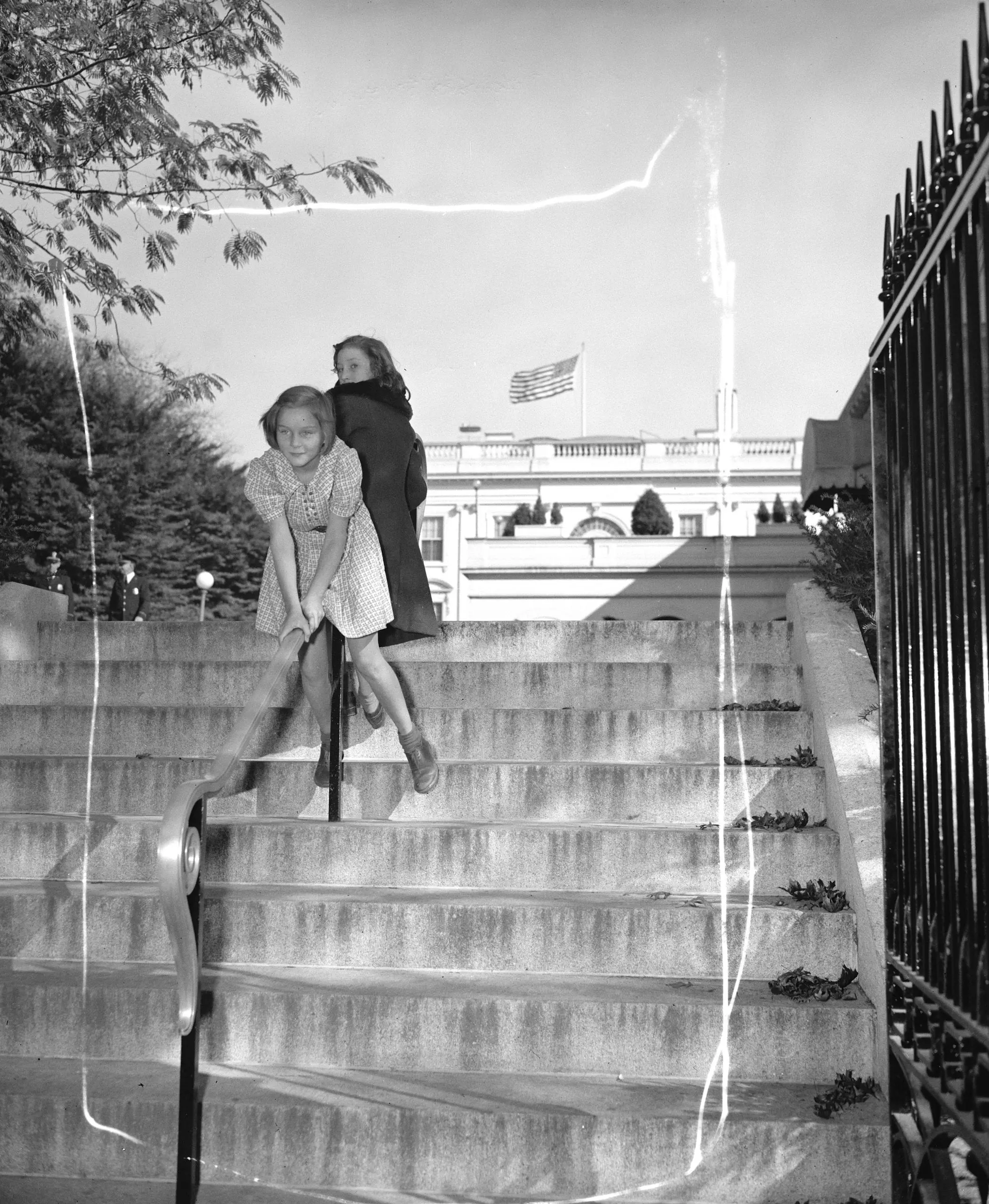 This is a very important picture. Washington, D.C., Oct. 27. A photographer was covering the White House yesterday, snapping pictures of important men after they had conferred with President Roosevelt on his way back to the laboratory he happened to notice thse two little girls, Patricia Freeman and Frances Gross, having fun sliding on the new railing that leads up to the executive offices. Anything around the White House thats new, makes news, the editor though so too and also an very important one becuse there are very few other Capitol cities on this troubled globe where it would catch a photorgapher's eye, Imagine Berlin, or Rome. Imagine even Buckingham Palace, imagine the palaces of rulers the world around, and then try to imagine two little girls having fun sliding on a railing. SS Troopers in Berlin, Grenadiers at Buckingham--verboten-you can't do this you know, vigorous shooing away from the Plazzo Venesia in Rome. But here the little girls slide down the railing an it doesn't seem to affect the affairs and progress of government and as long as the little girls can keep on at their fun, our president and our government are safer for us than if all the SS troopers in the world stood by to make it so, 10-27-38