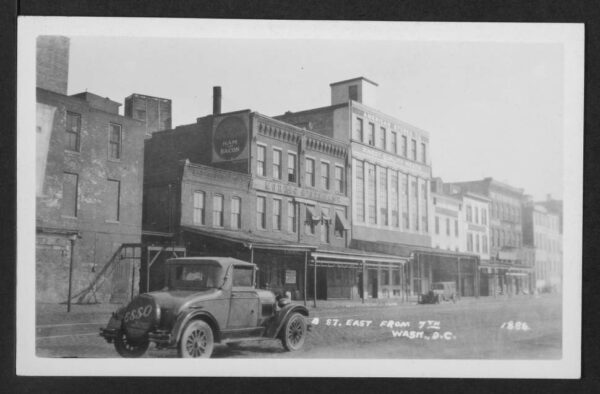 View of commercial building on the northeast corner of B Street (later Constitution Avenue) and 7th Street NW. An automobile in the foreground has an Esso advertising cover on its spare tire that reads, "ESSO THE GIANT POWER FUEL." - February 1st, 1931