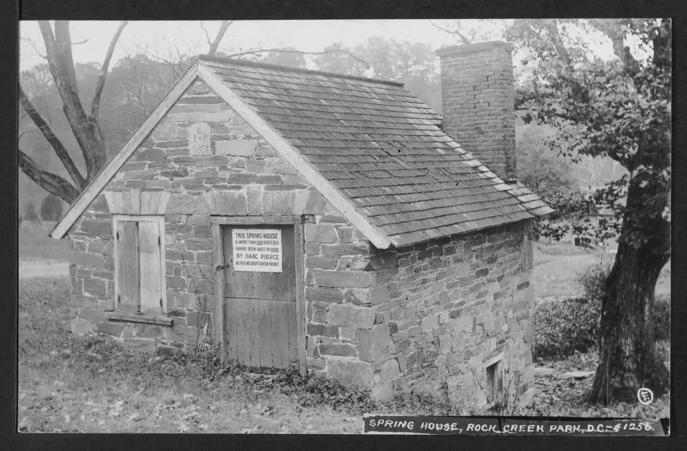 Close up view of east and north elevations of the Rock Creek Park spring house. Affixed to the building door is a sign that reads "This spring house is more than 100 years old having been built in 1801 by Isaac Pierce as per inscription on front."