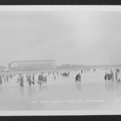 View looking east from the middle of a frozen Tidal Basin upon which many individuals are walking or skating. The Bureau of Engraving and Printing is visible in the distance.