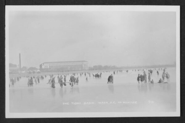 View looking east from the middle of a frozen Tidal Basin upon which many individuals are walking or skating. The Bureau of Engraving and Printing is visible in the distance.