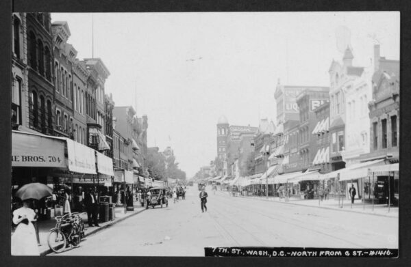 View looking north up 7th Street NW from G Street NW. Streetcars, automobiles and horse pulled carts are in the street.