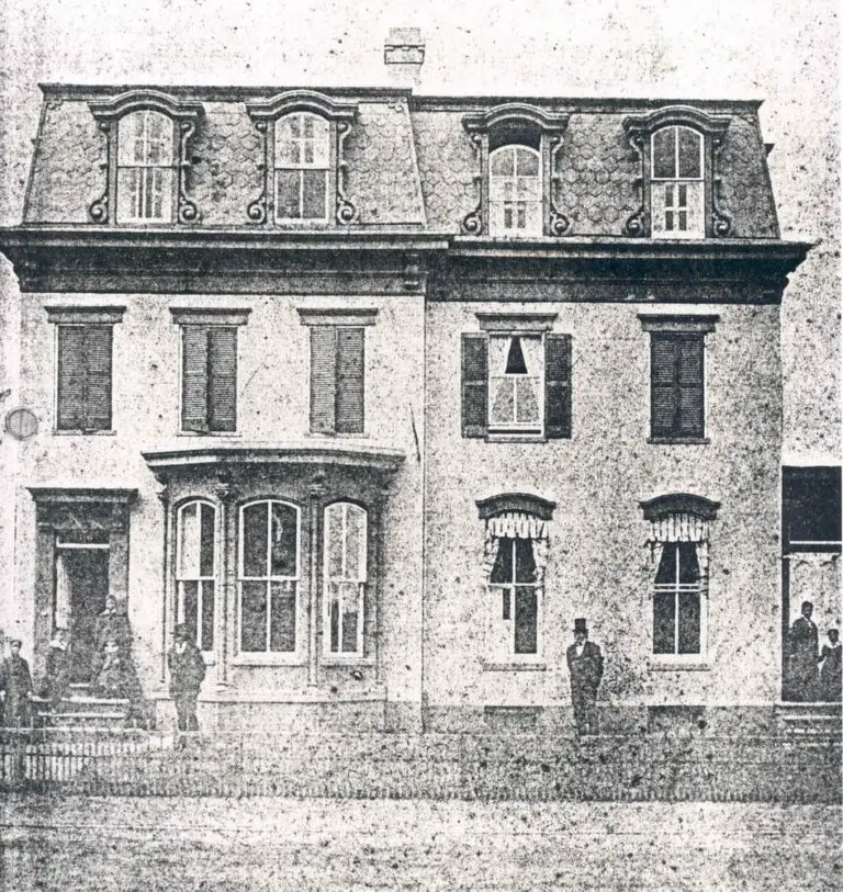 1876. Photographer: W.W. Core, Washington, D.C. Frederick Douglass is standing on the front lawn of his home on A Street, N.E., Washington, D.C. Other family members are standing out on the front porch on both side of the houses.