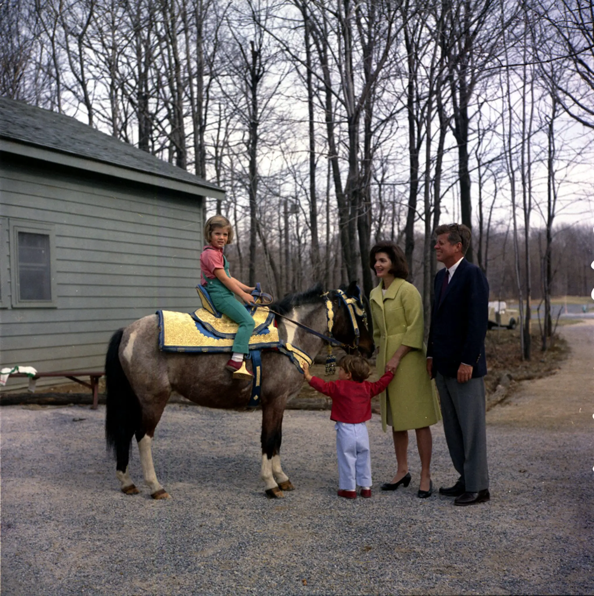 31 March 1963 President John F. Kennedy and family watch Caroline Kennedy riding a horse named "Tex" at Camp David.  "Tex" is wearing a blue and gold Moroccan saddle, a gift to President Kennedy from King Hassan II.  Photograph includes: (L-R) Caroline Kennedy, John F. Kennedy, Jr., First Lady Jacqueline Kennedy, and President Kennedy.  Camp David, Maryland.  Please credit "Robert Knudsen, White House/John F. Kennedy Presidential Library and Museum, Boston"