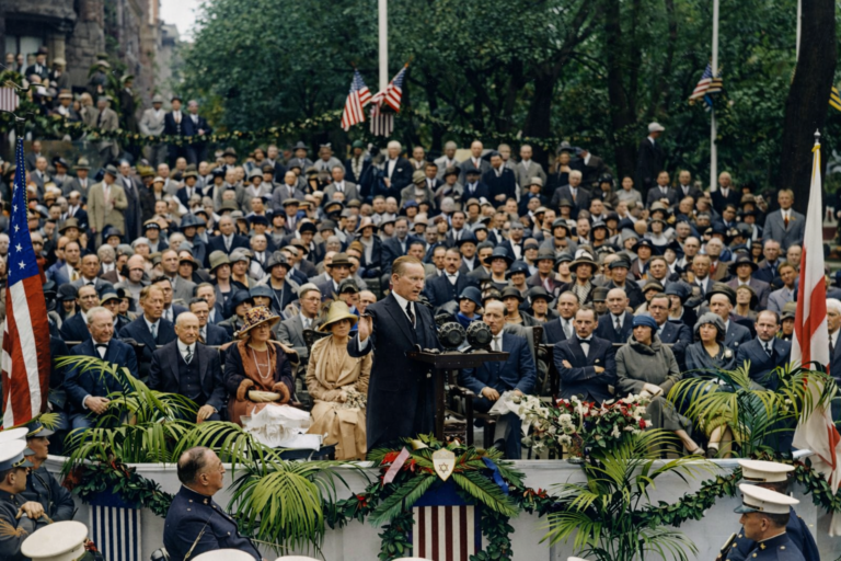 President Calvin Coolidge stands at a platform addressing a crowd at the 1925 cornerstone ceremony, with a band in the foreground