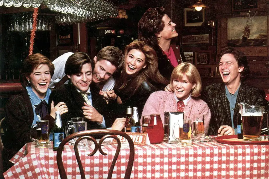 A group shot from the film 'St. Elmo’s Fire' showcasing its seven lead actors—Rob Lowe, Demi Moore, Emilio Estevez, Ally Sheedy, Mare Winningham, Judd Nelson, and Andrew McCarthy. They are all dressed in college graduation attire, symbolizing the transition into adulthood. Their expressions and body language reflect a sense of unity, camaraderie, and hopeful anticipation towards the future. The image captures the essence of the film's theme about the complexities and beauty of post-college friendships.