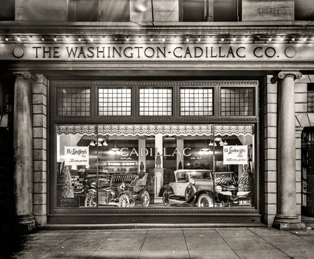 A black and white photograph from 1927 showing the interior of the Washington-Cadillac showroom on Connecticut Avenue in Washington, D.C. On the left is a vintage Cadillac, and on the right is the new LaSalle, marking its first year as Cadillac's "companion make." This image was captured on a National Photo Company glass negative.