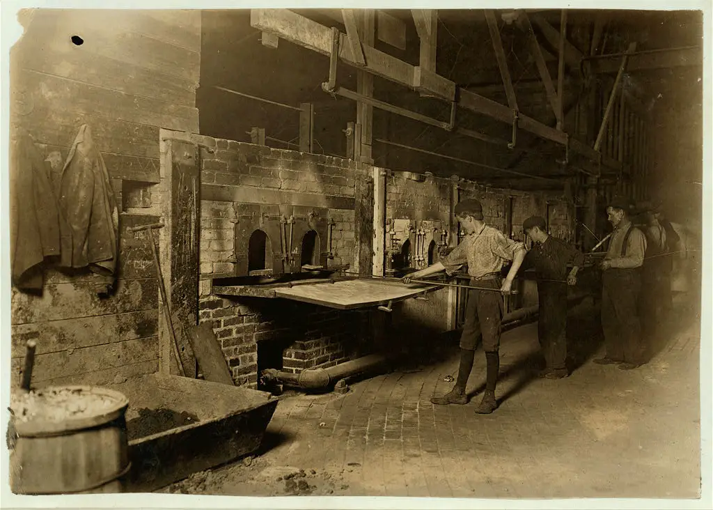 Photograph by Lewis Wickes Hine from October 1908, titled 'Midnight in a Glass Works' in Grafton, West Virginia. The image, denoted as photo 162, likely depicts the interior of a glass factory with the workers present during a night shift.