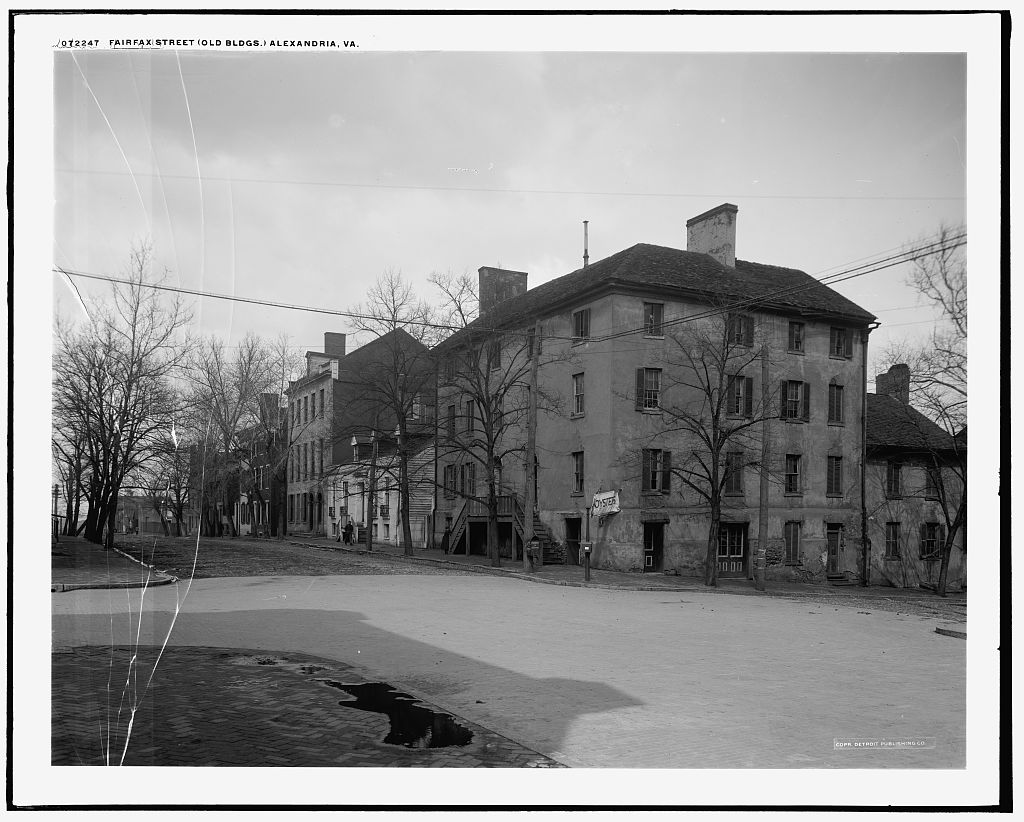 Row of historic brick and clapboard buildings along Fairfax Street in Alexandria, Virginia, photographed between 1910 and 1920.