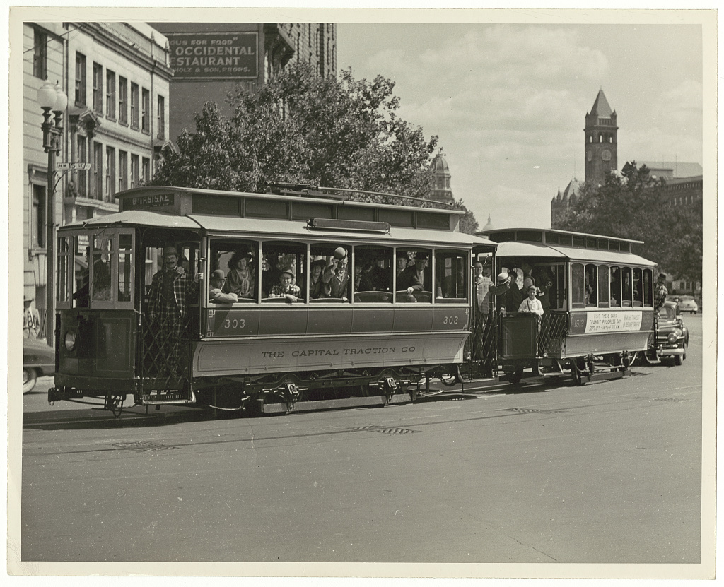 A vintage open-sided Capital Traction Company trolley car number 303 on a 1949 tourist excursion on 15th Street NW in Washington DC, with the Old Post Office clock tower in the background