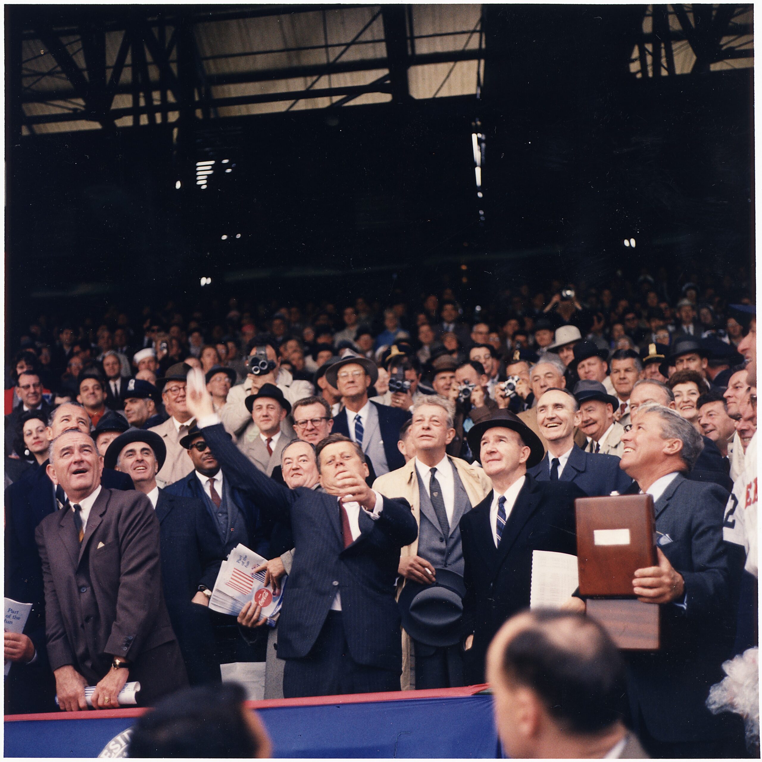Kennedy throws the first pitch at Griffith Stadium on Opening Day 1961 with LBJ and Dave Powers beside him.