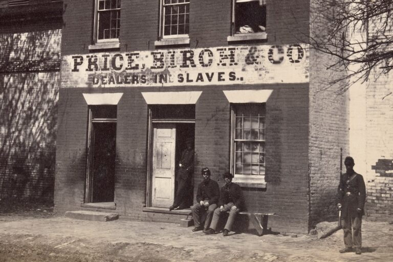 Black and white 1863 photograph by Andrew J. Russell showing a Union soldier standing in front of the Price, Birch and Co. Dealers in Slaves building at 1315 Duke Street, Alexandria, Virginia