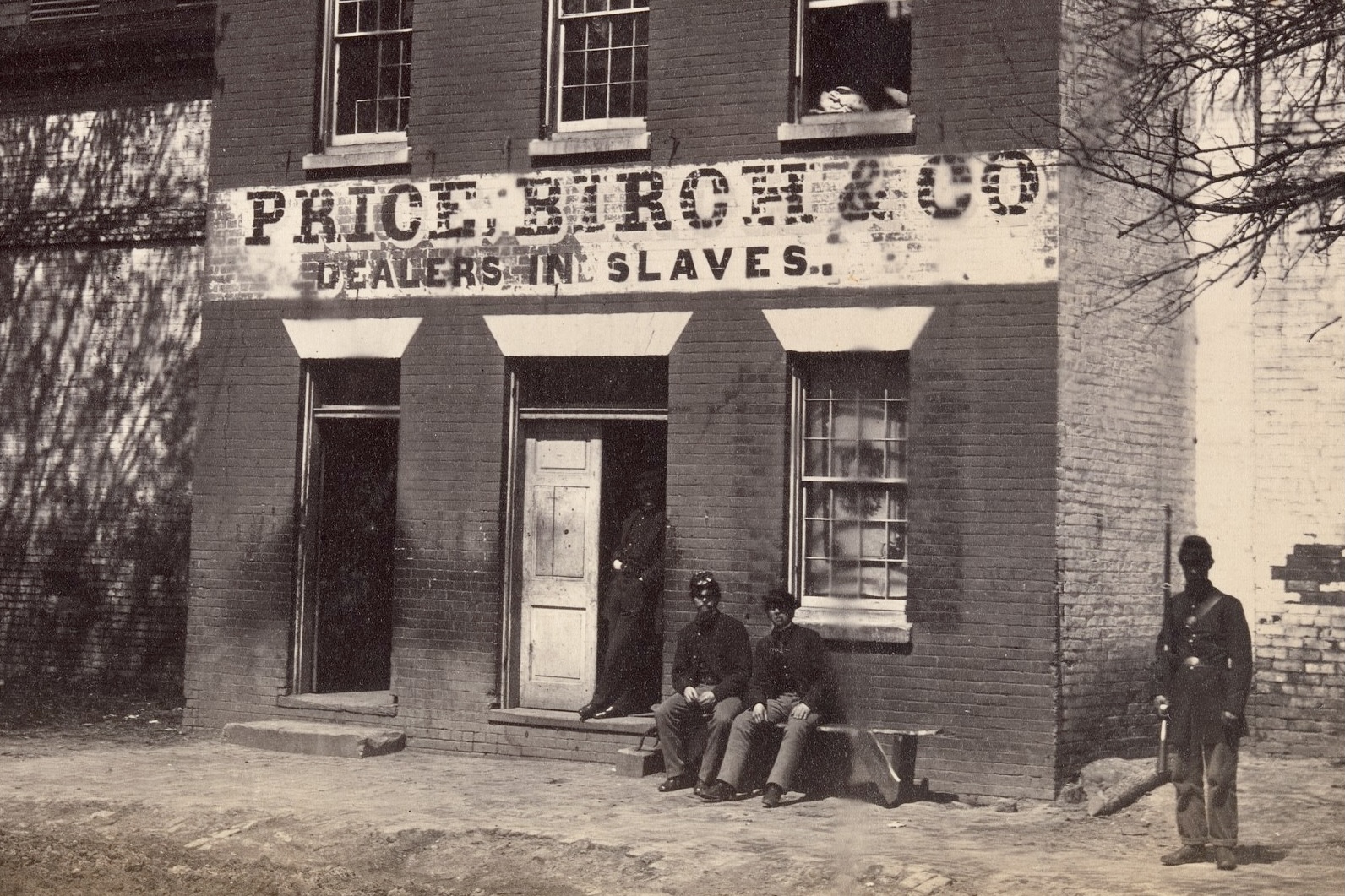 Black and white 1863 photograph by Andrew J. Russell showing a Union soldier standing in front of the Price, Birch and Co. Dealers in Slaves building at 1315 Duke Street, Alexandria, Virginia