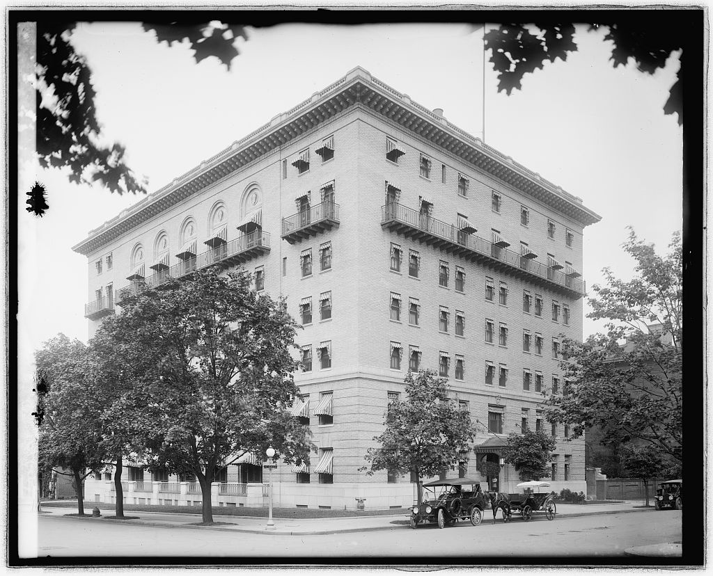 Summer view of the 1912 Army and Navy Club building with trees in leaf and two automobiles at the entrance