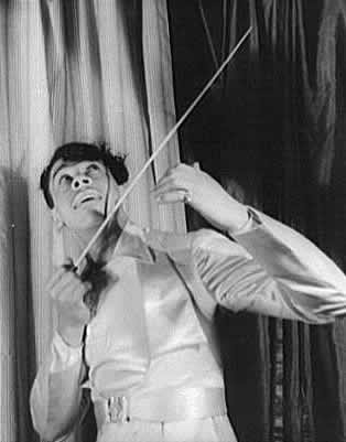 Black-and-white photograph of Cab Calloway, dressed in a white suit, raising a conductor's baton dramatically while leading his band.