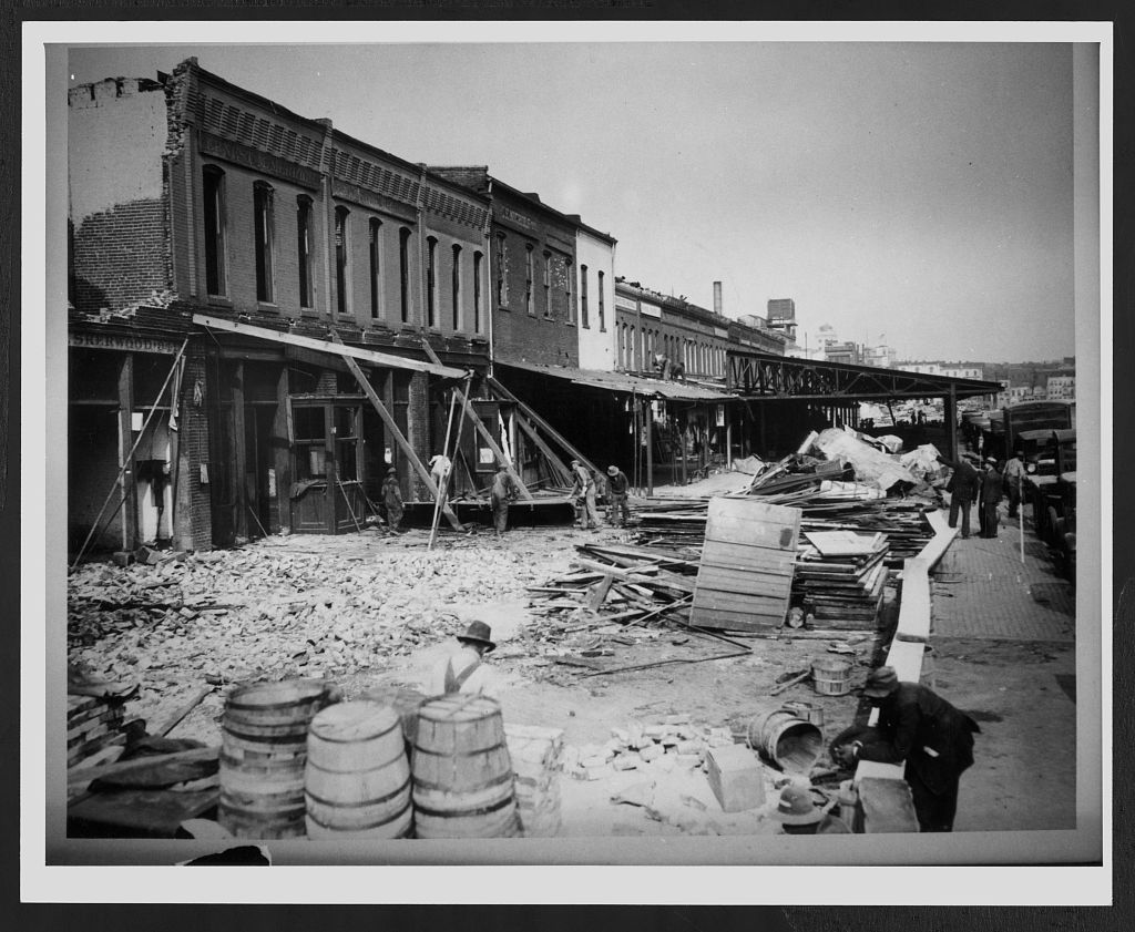 Demolition of the western wing of Center Market in 1930, with one tower and a stretch of facade still standing while crews work to take it down.