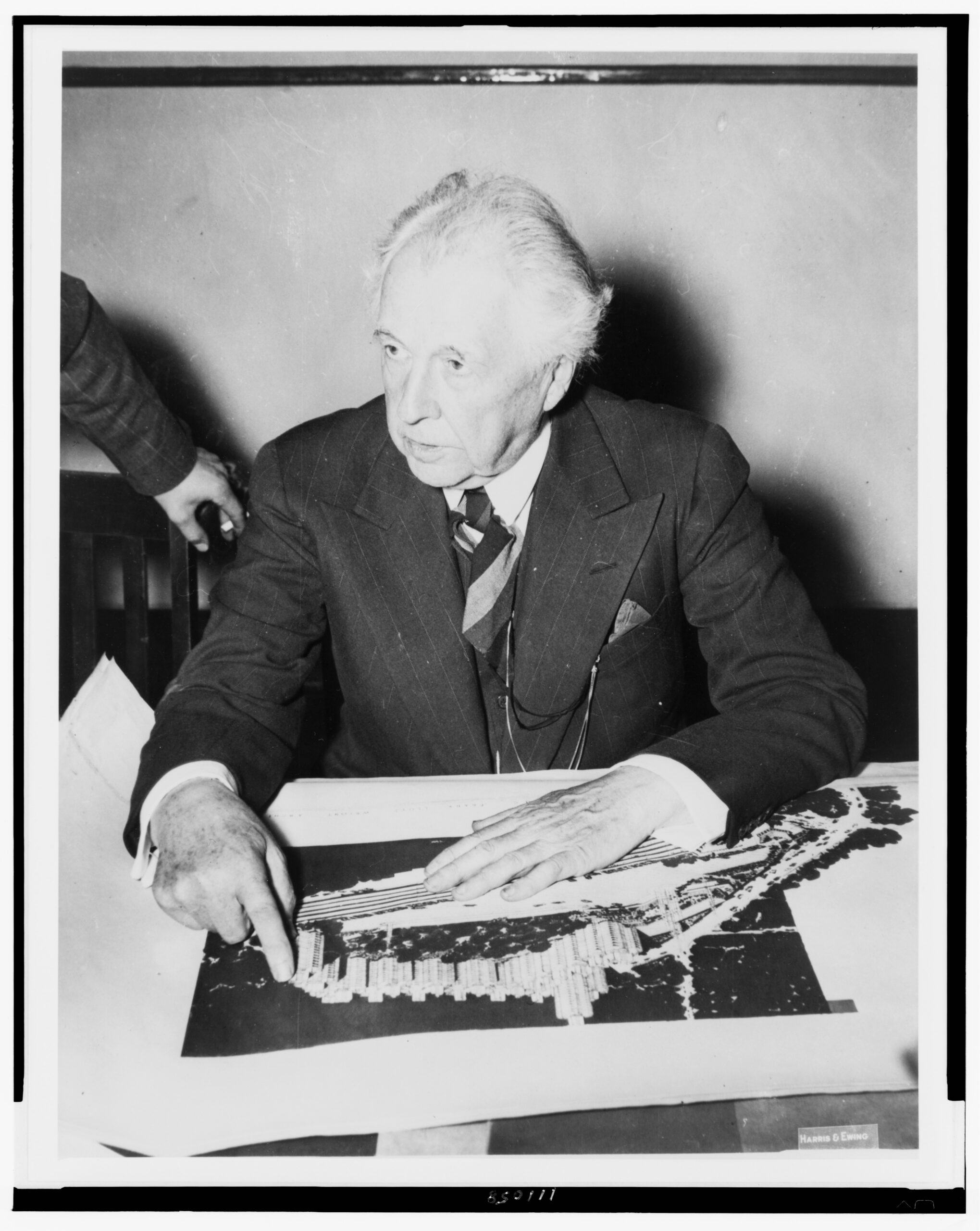 Frank Lloyd Wright seated and pointing to his design for Crystal Heights, photographed in 1940