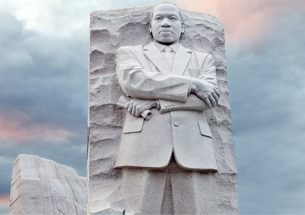 The Stone of Hope sculpture of Martin Luther King Jr. rises from a granite plinth on the north bank of the Tidal Basin, with cherry trees in the background.