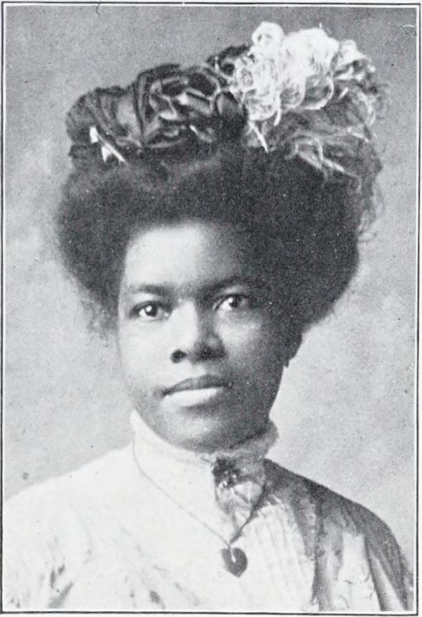 Black-and-white portrait of Nannie Helen Burroughs, a young Black woman with an elaborate floral headdress and a high collar, photographed in the early 1900s.