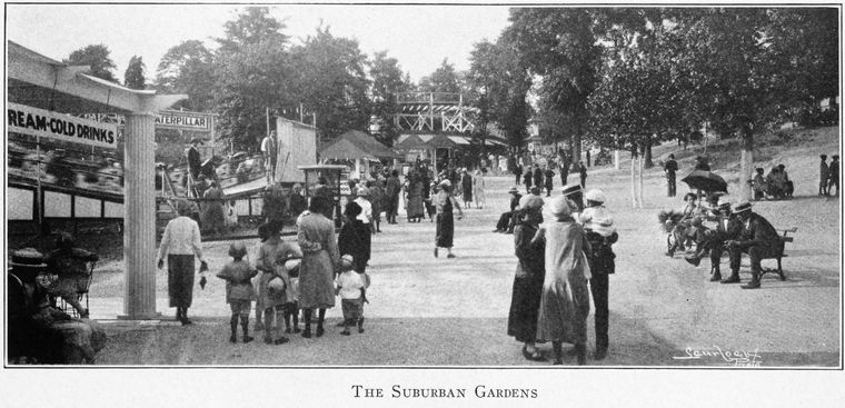 Black-and-white panoramic photograph from 1927 of Suburban Gardens amusement park, showing a sign reading ICE CREAM COLD DRINKS at left, a CATERPILLAR ride sign behind it, and Black families in summer dress walking along a tree-lined dirt path.