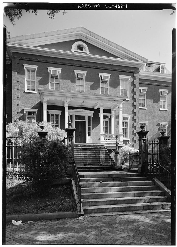 Black and white photo of the Old Naval Hospital's Italianate central pavilion and entrance portico behind a cast-iron fence