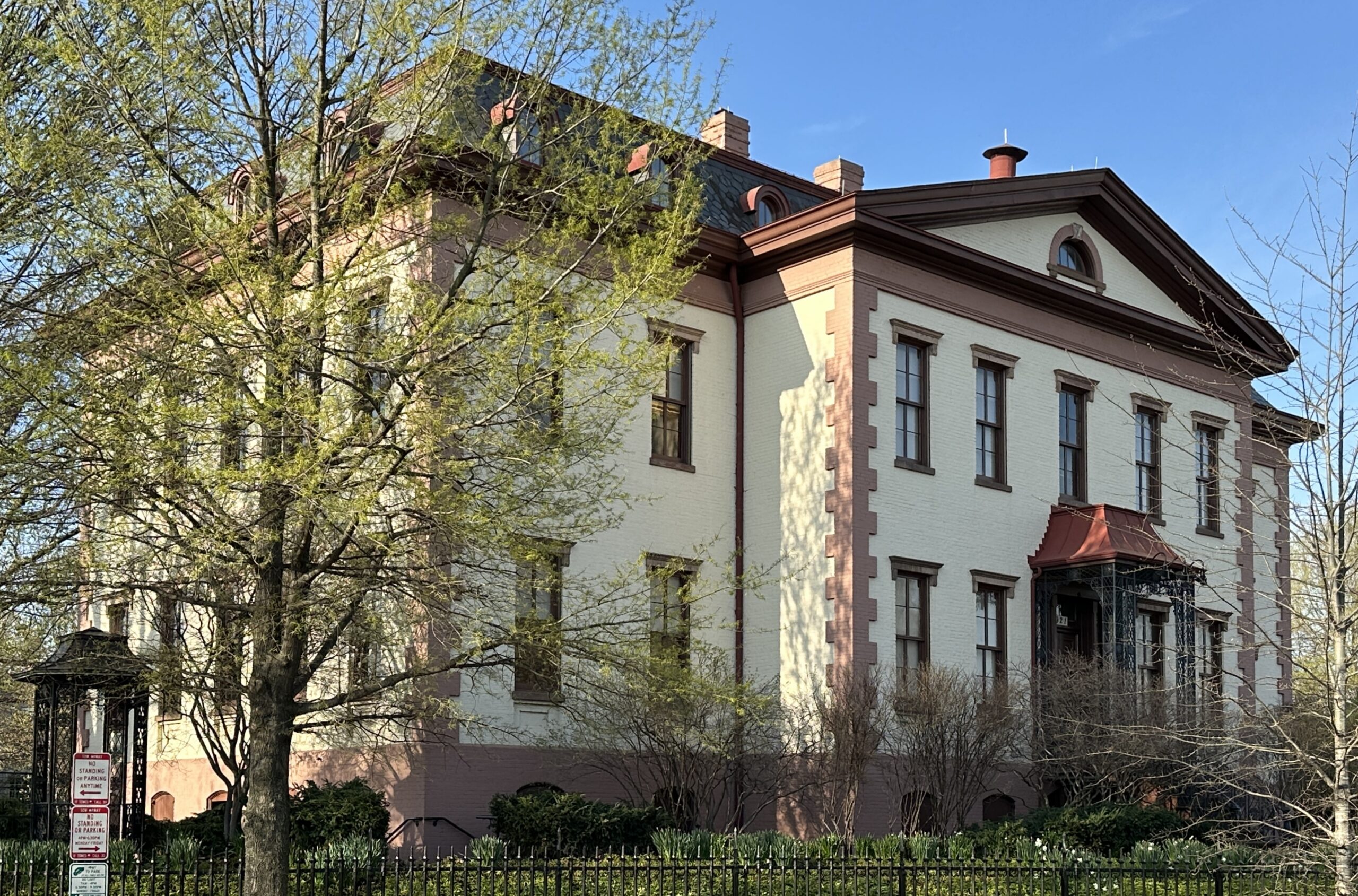 Color photo of the restored Old Naval Hospital, now Hill Center, in cream and brown with its iron fence and surrounding trees