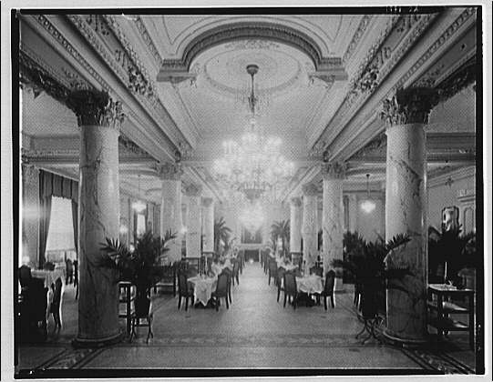 Columned dining room of the Raleigh Hotel with crystal chandelier and white linen tables