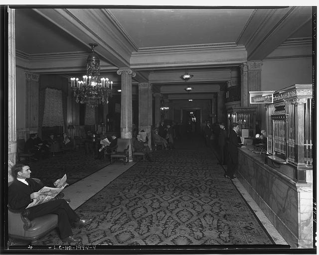 A man in a suit reads a newspaper in the marble-columned lobby of the Raleigh Hotel