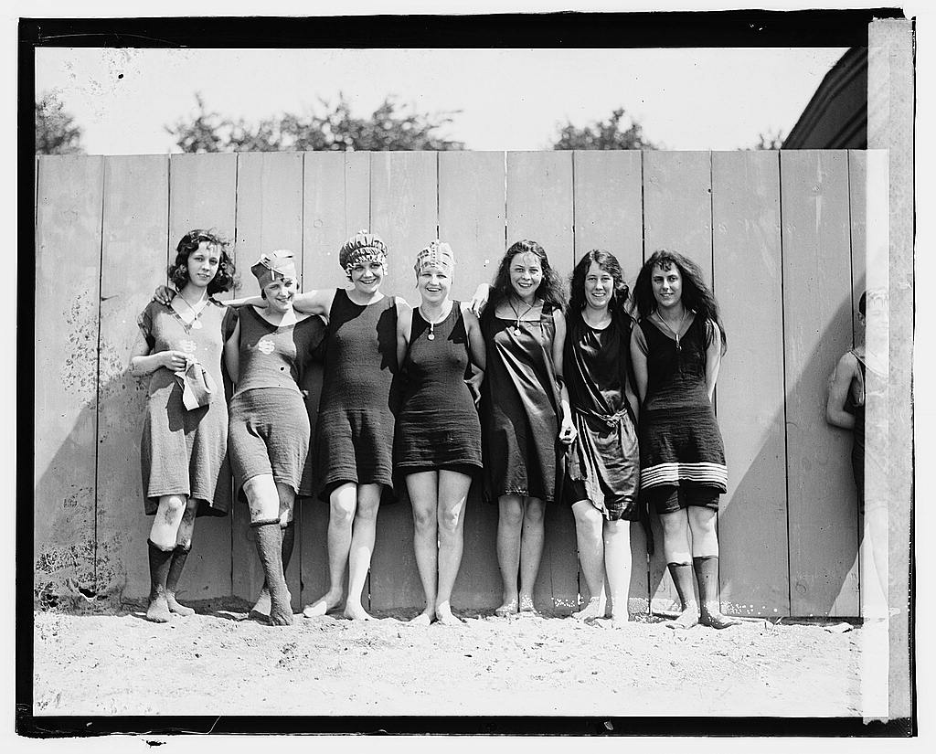 A row of about ten women in early 1920s bathing suits and caps stand on the sand at the Tidal Basin.