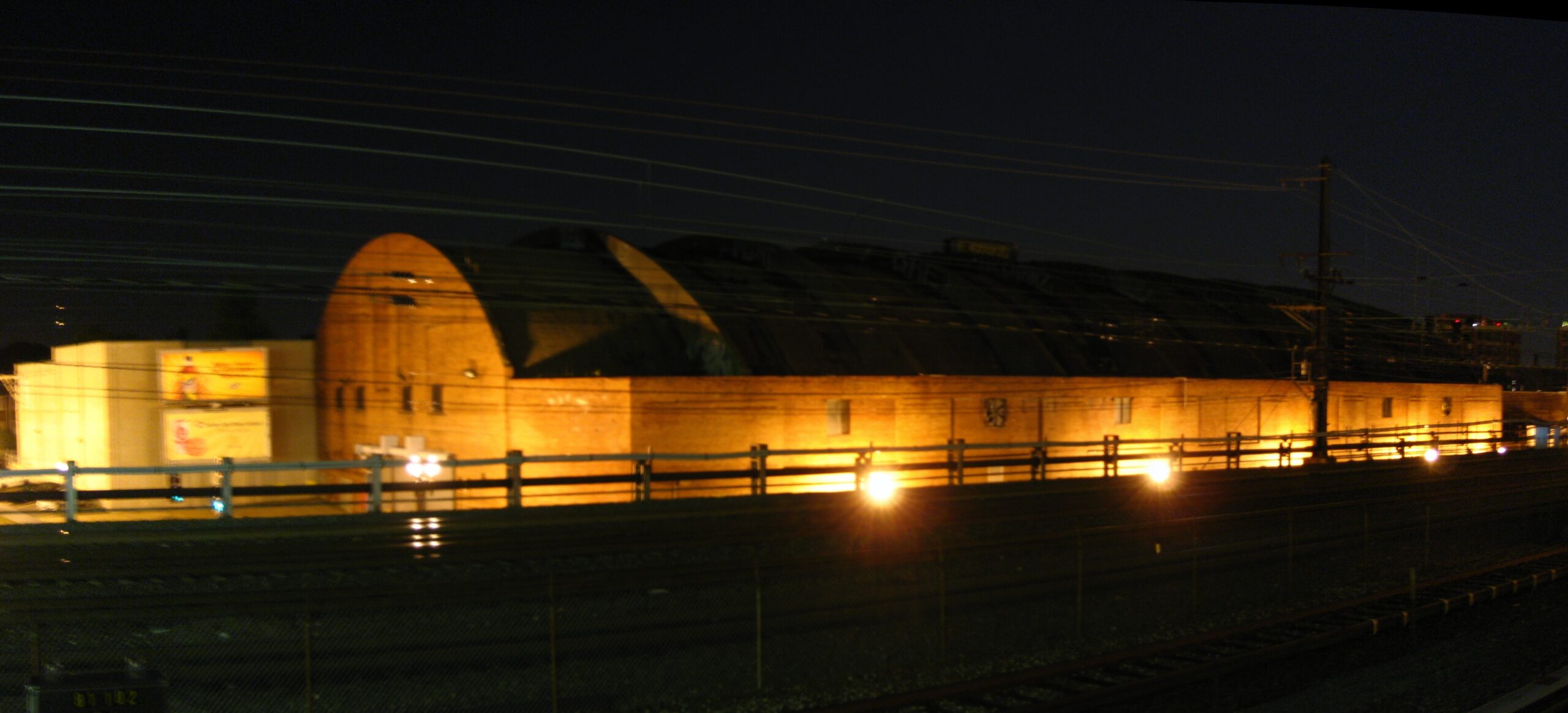 Washington Coliseum exterior at night in 2008, with low golden floodlights and an Amtrak train passing on the tracks behind it.