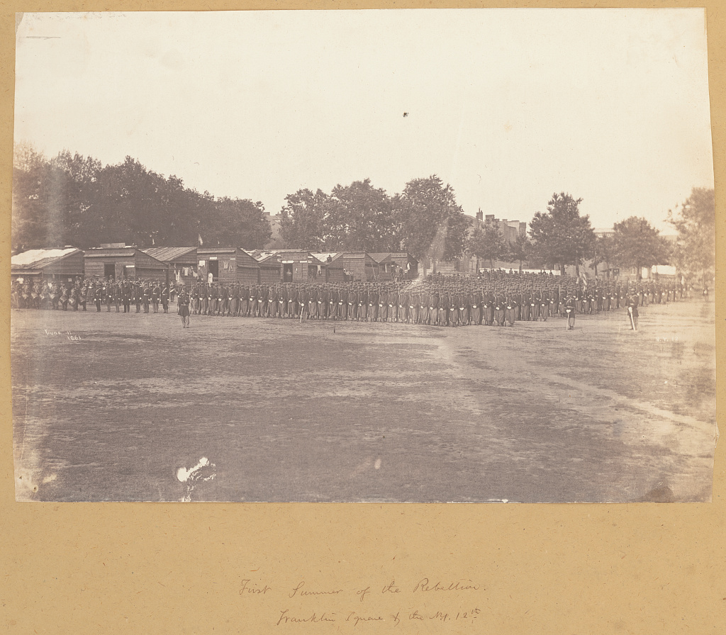 Soldiers of the 12th New York State Militia in formation at Franklin Square in 1861, with wooden barracks behind them