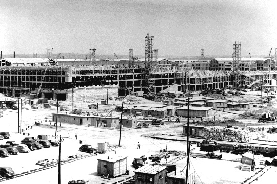 Pentagon construction site on July 1, 1942, with three sides framed up, parked cars and worker trailers in the foreground, and the fifth side still open ground