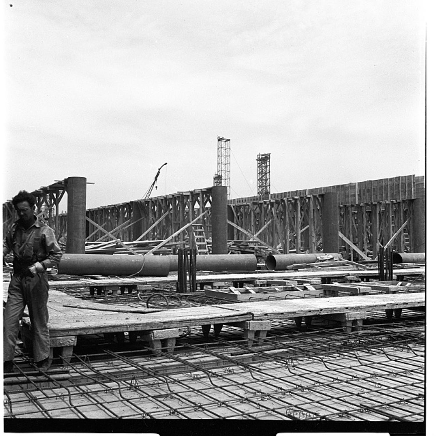 A worker walks across the rebar grid for a Pentagon floor slab as concrete forms and lifting towers rise in the background, 1942