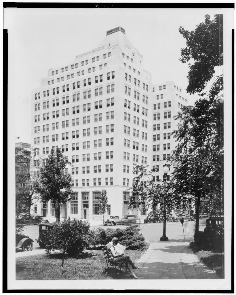 Woman reading on a bench in Franklin Square in 1929 with the Tower Building at 14th and K Streets behind her
