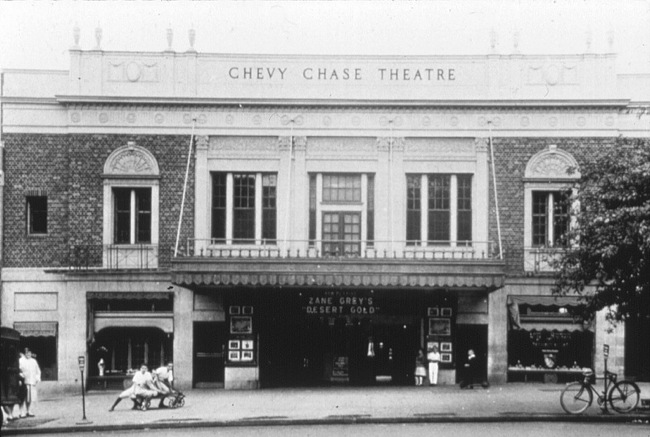 Black and white photograph of the Chevy Chase Theatre showing Zane Grey's Desert Gold on the marquee, with people sitting on a bench and a bicycle at the curb.