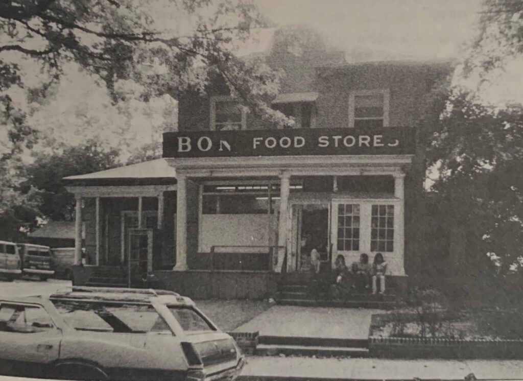 The cream and white two-story frame corner market at 5608 Broad Branch Road NW, with a broad front porch and a hanging Market sign, kids and shoppers gathered outside on a winter afternoon.