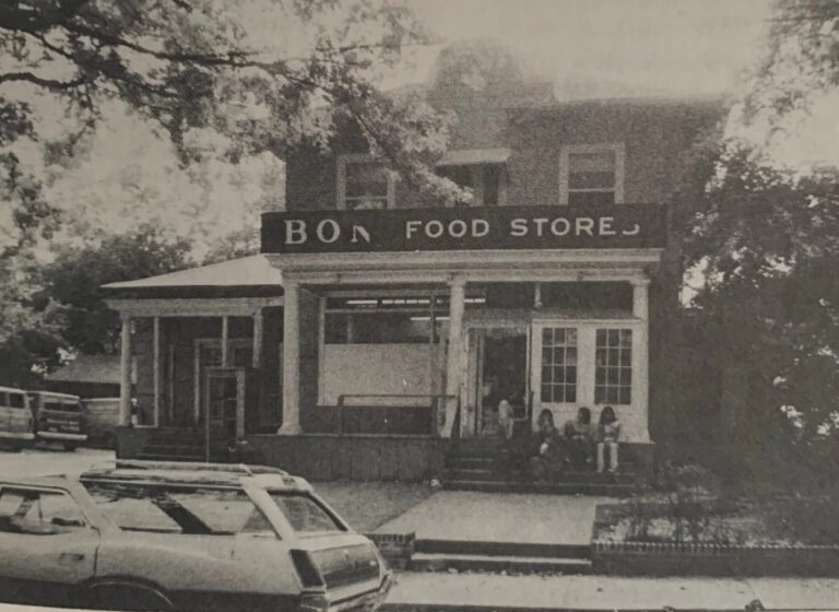 The cream and white two-story frame corner market at 5608 Broad Branch Road NW, with a broad front porch and a hanging Market sign, kids and shoppers gathered outside on a winter afternoon.