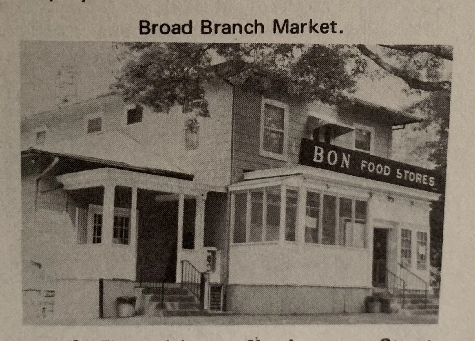 Black and white vintage photograph of the corner store labeled BON FOOD STORES on the marquee, with the same two-story frame building and porch that stands today.