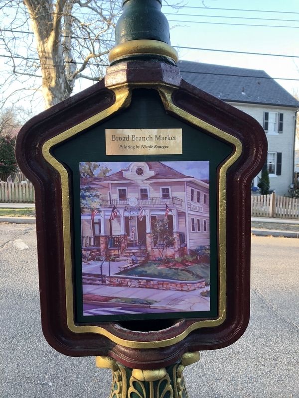 A restored ornamental cast iron DC call box mounted on a post at the corner of McKinley Street and Broad Branch Road NW, painted maroon and gold and displaying a watercolor painting of the market by Nicole Bourgea.