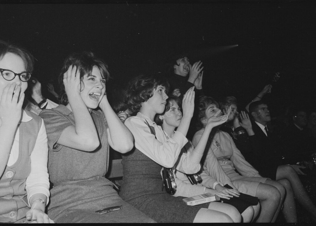 Teenage girls in the Coliseum crowd screaming with their hands pressed over their ears